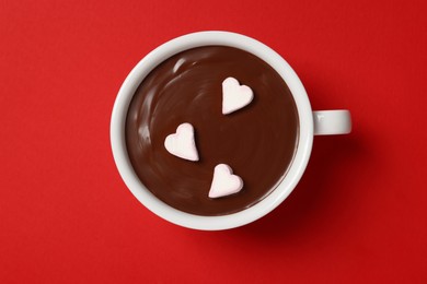 Cup of hot chocolate with heart shaped marshmallows on red background, top view