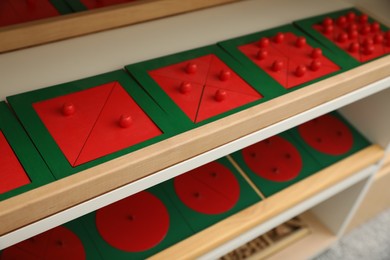 Photo of Wooden puzzles with different geometric shapes on shelves in room, closeup. Montessori toy