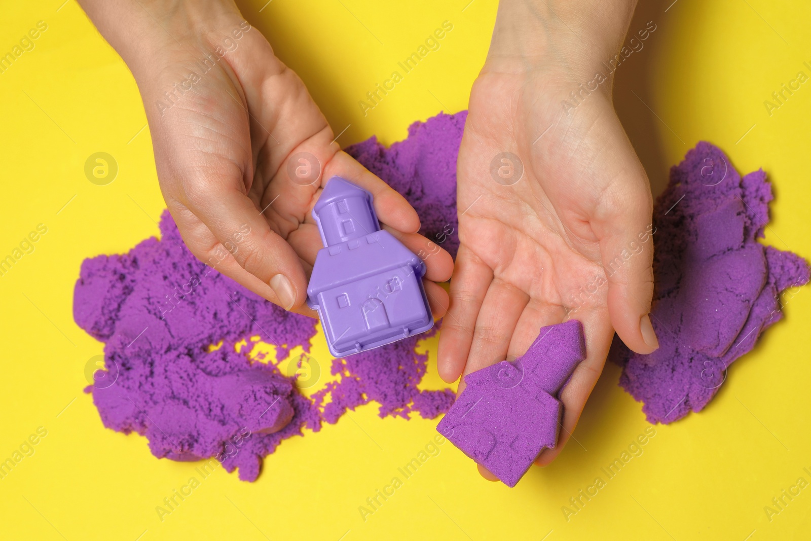 Photo of Woman playing with kinetic sand on yellow background, top view