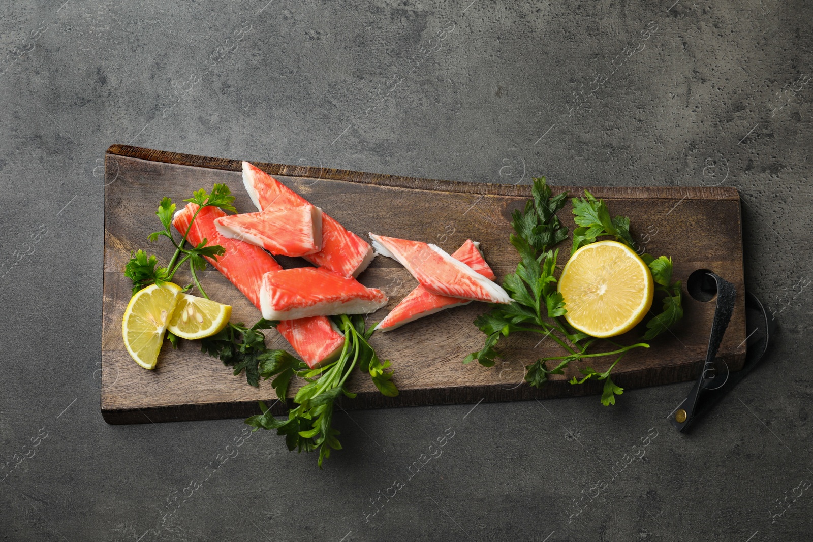 Photo of Cut crab sticks, lemon and parsley on grey table, top view