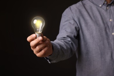 Photo of Glow up your ideas. Closeup view of man holding light bulb on black background