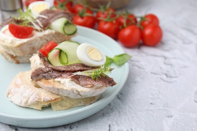 Photo of Delicious bruschettas with anchovies, tomato, cucumber, egg and cream cheese on white textured table. Space for text