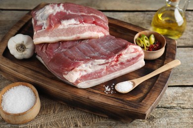 Photo of Pieces of raw pork belly, salt, oil, garlic and rosemary on wooden table