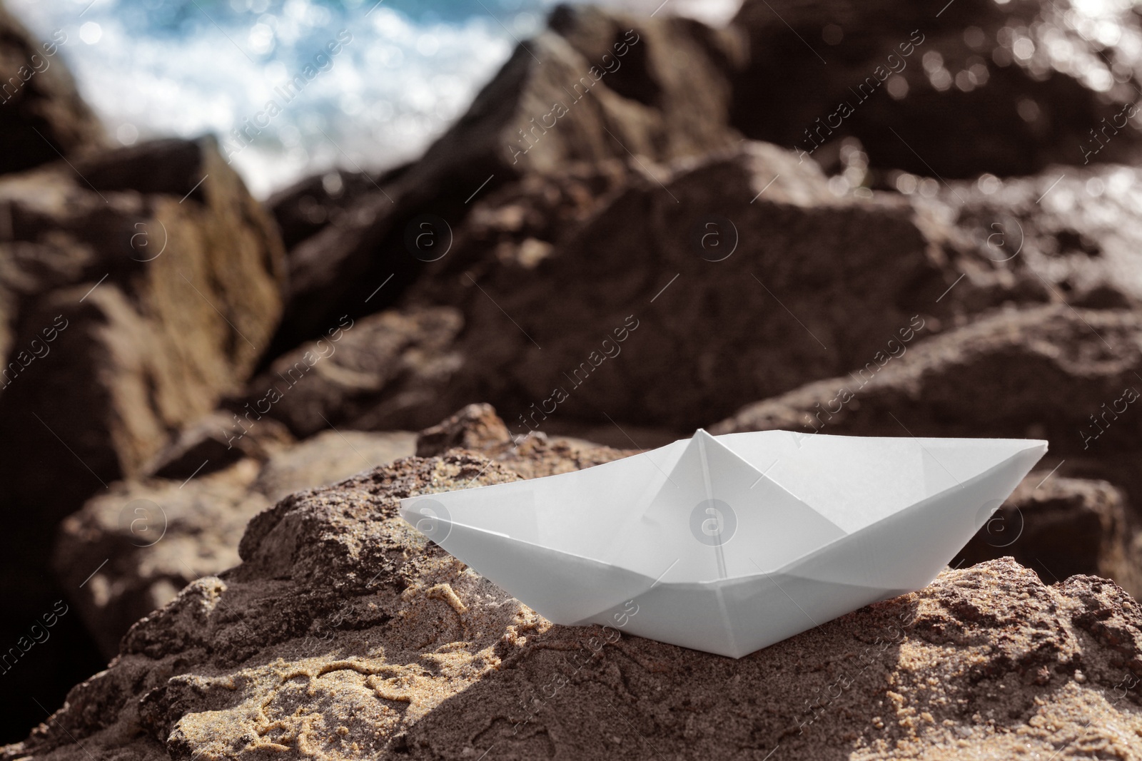 Photo of White paper boat on rock near sea. Space for text