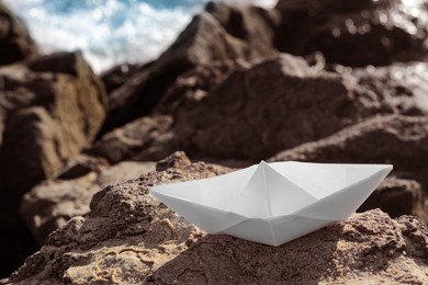 Photo of White paper boat on rock near sea. Space for text