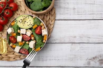 Bowl of tasty salad with tofu and vegetables on white wooden table, flat lay. Space for text