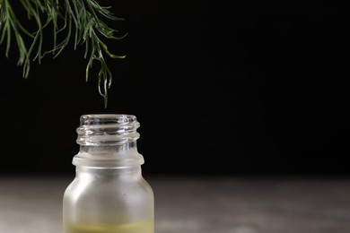 Dripping essential oil from dill into bottle against black background, closeup. Space for text