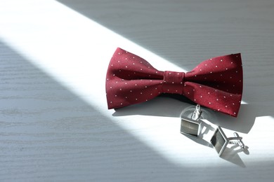 Photo of Stylish red bow tie and cufflinks on white wooden table. Space for text