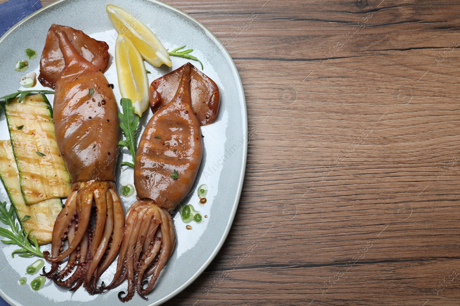 Photo of Delicious grilled squids served on wooden table, top view. Space for text