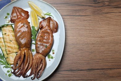 Delicious grilled squids served on wooden table, top view. Space for text