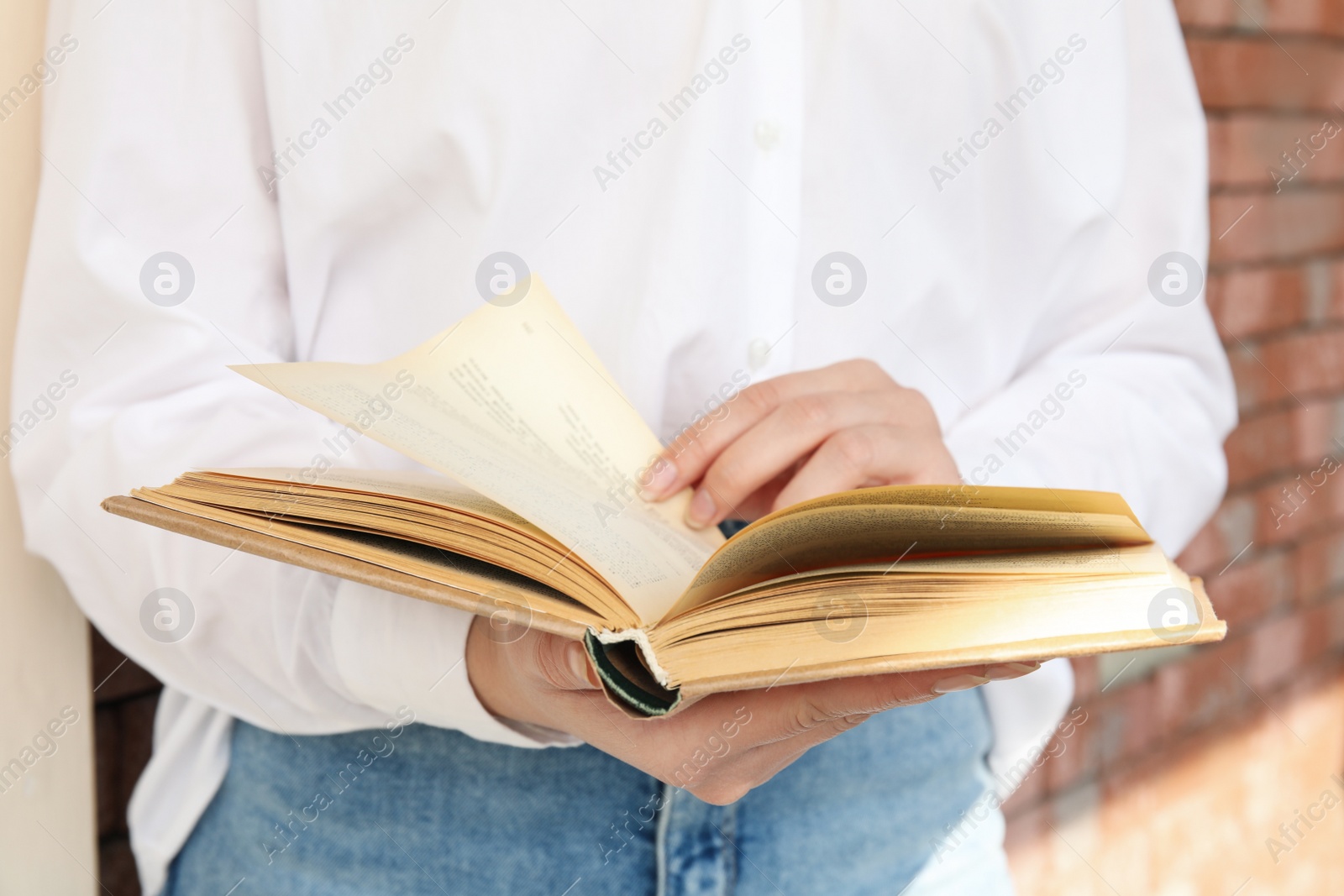 Photo of Woman reading book near brick wall outdoors, closeup