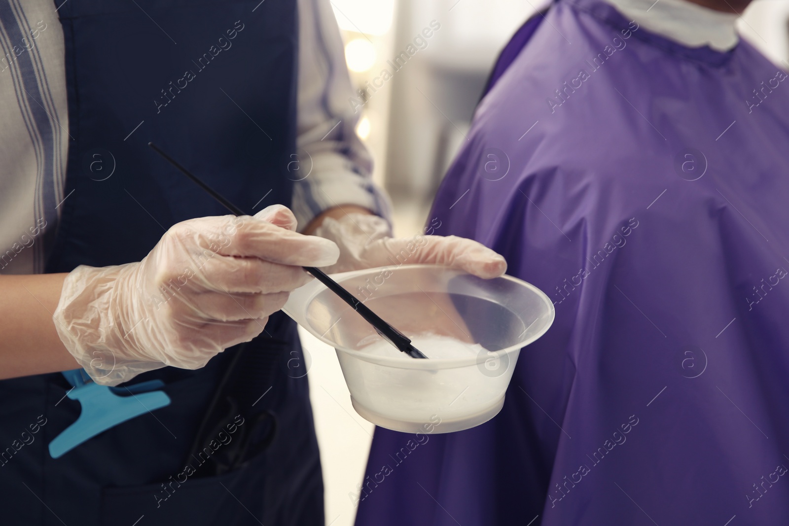 Photo of Professional hairdresser holding bowl with hair dye in beauty salon, closeup