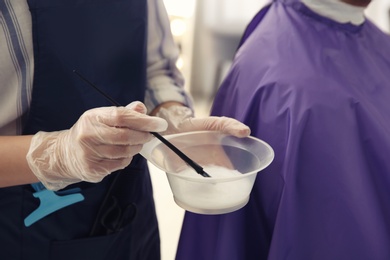 Photo of Professional hairdresser holding bowl with hair dye in beauty salon, closeup