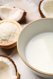 Photo of Bowl of delicious coconut milk, flakes and coconuts on white table