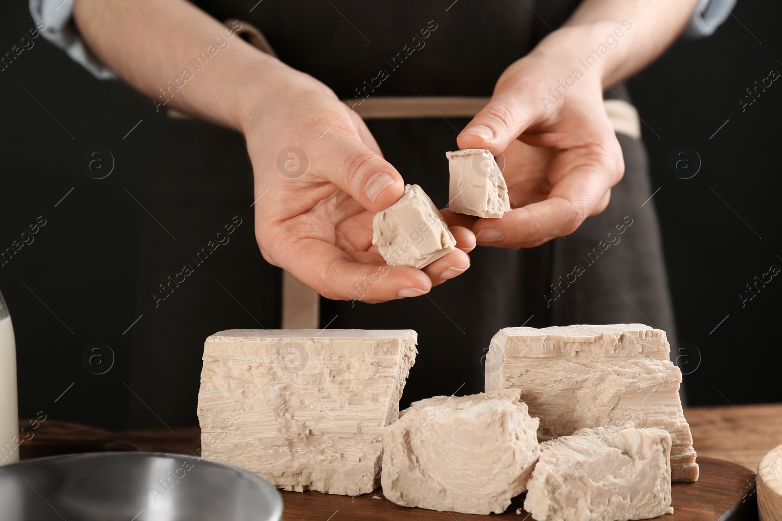 Photo of Woman with pieces of compressed yeast at wooden table, closeup