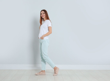 Young woman in stylish jeans near light wall. Space for text