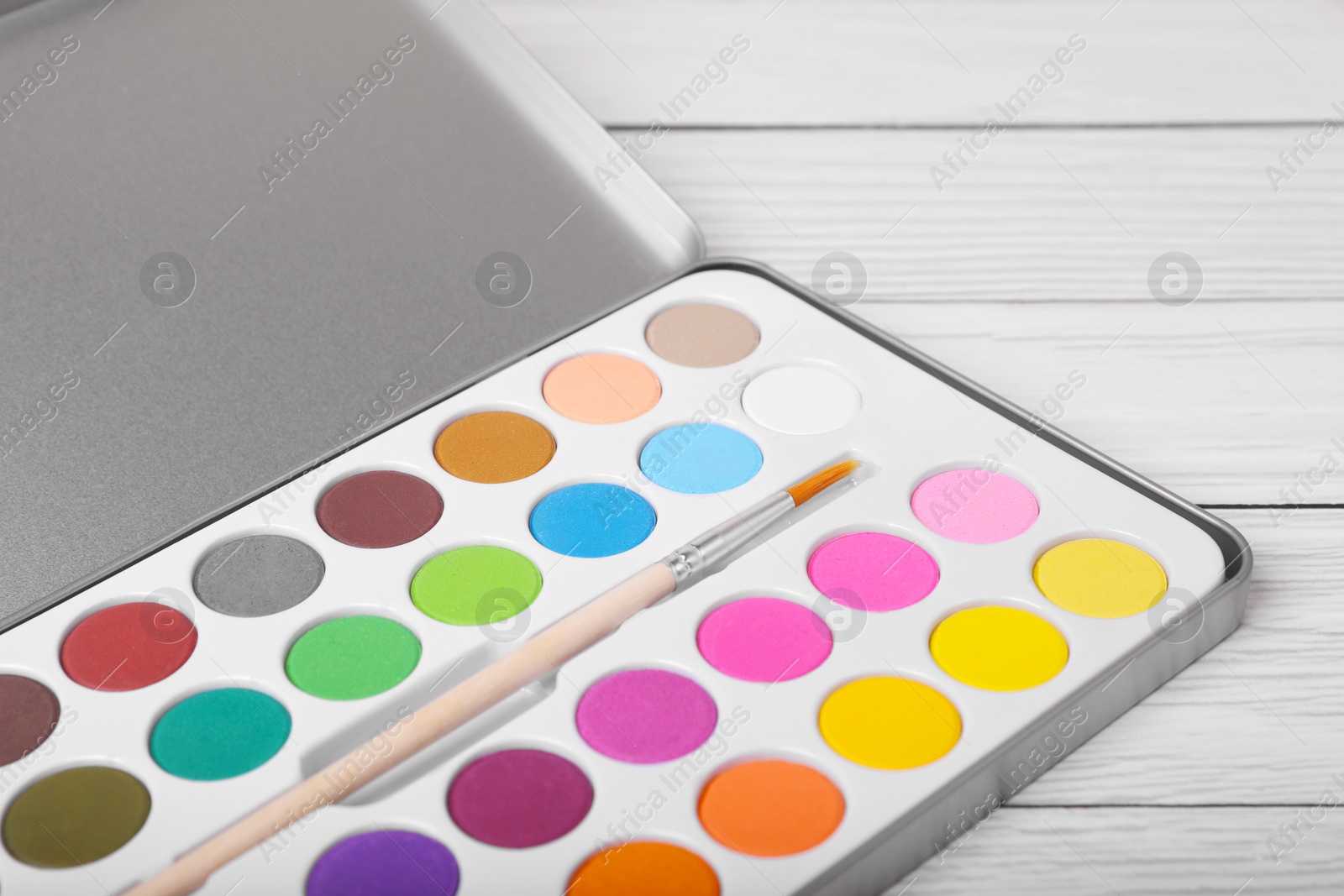 Photo of Watercolor palette with brush on white wooden table, closeup