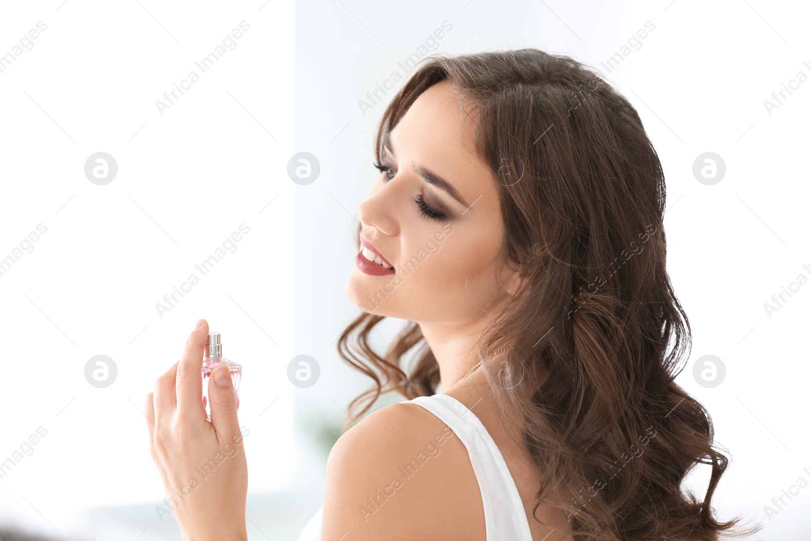 Photo of Beautiful young woman with bottle of perfume on blurred background