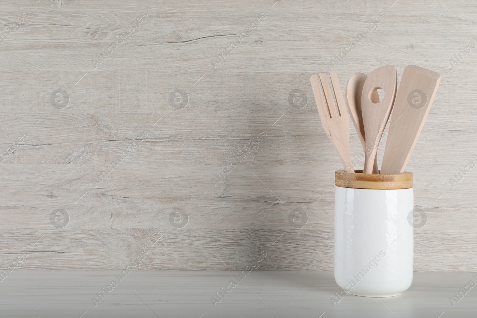 Photo of Holder with different kitchen utensils on white wooden table. Space for text