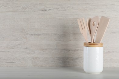 Photo of Holder with different kitchen utensils on white wooden table. Space for text