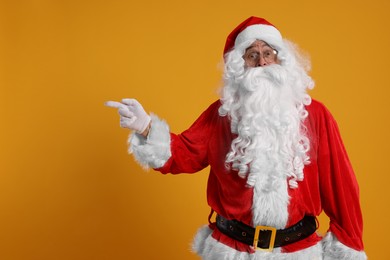 Photo of Merry Christmas. Santa Claus pointing at something on orange background, space for text