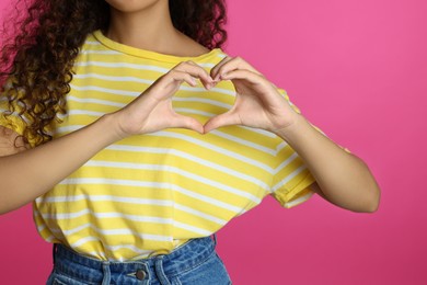 African-American woman making heart with hands on pink background, closeup