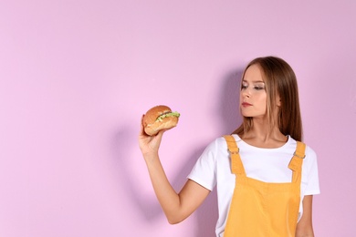 Slim woman with burger on color background. Healthy diet