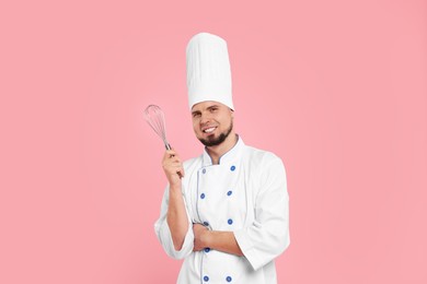 Photo of Happy professional confectioner in uniform holding whisk on pink background