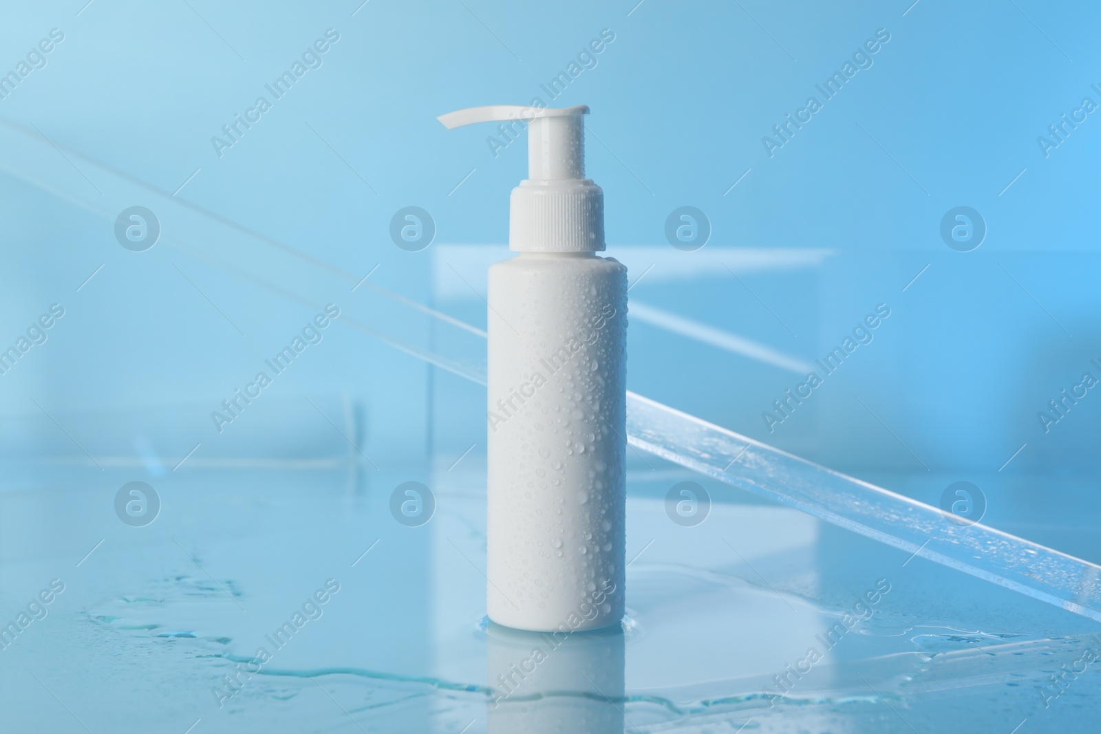 Photo of Wet bottle of face cleansing product on light blue background