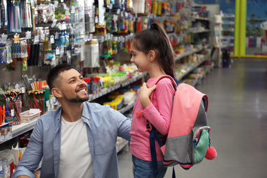 Photo of Little girl with father choosing school stationery in supermarket