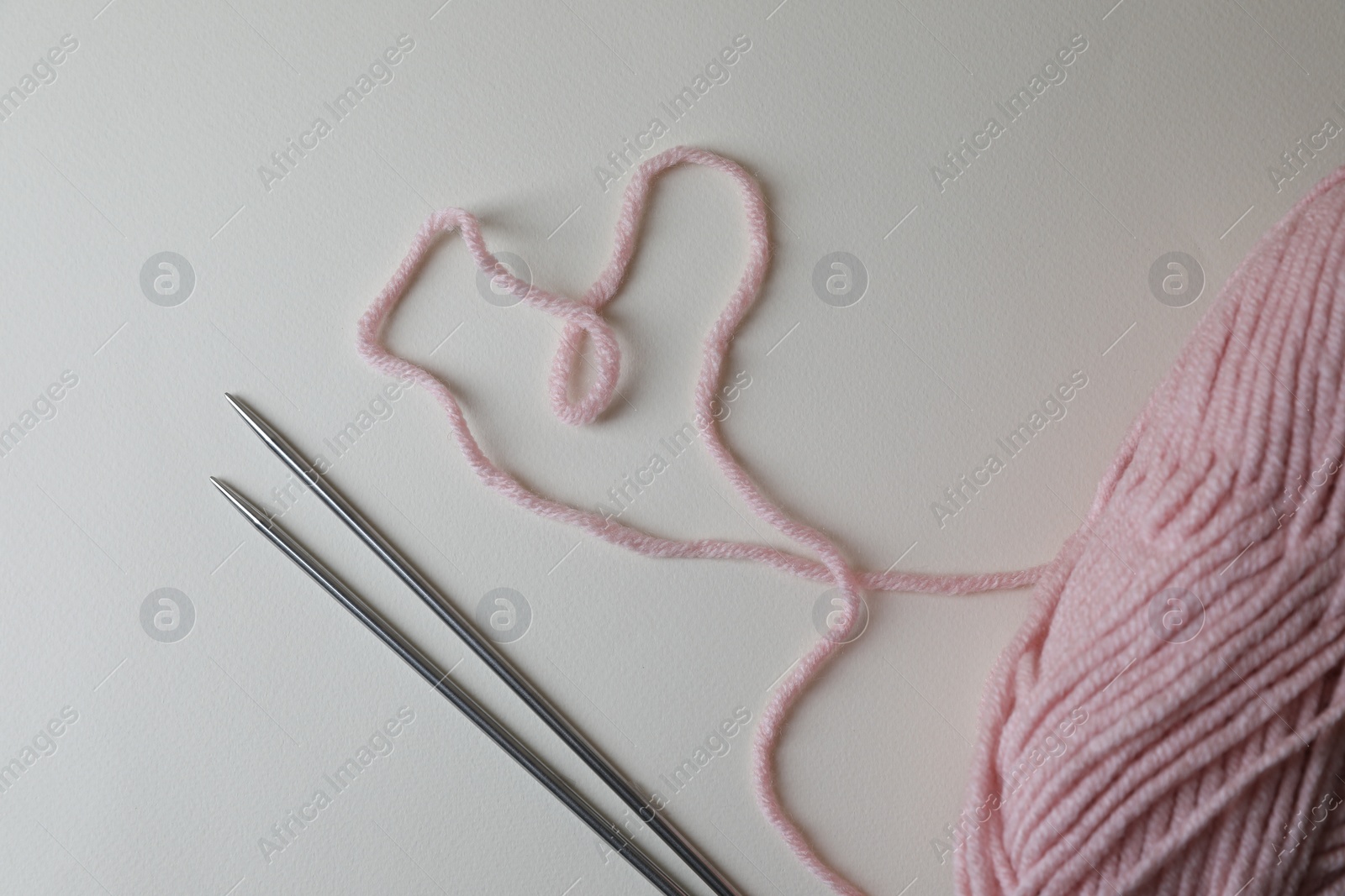 Photo of Soft pink yarn and metal knitting needles on light background, top view