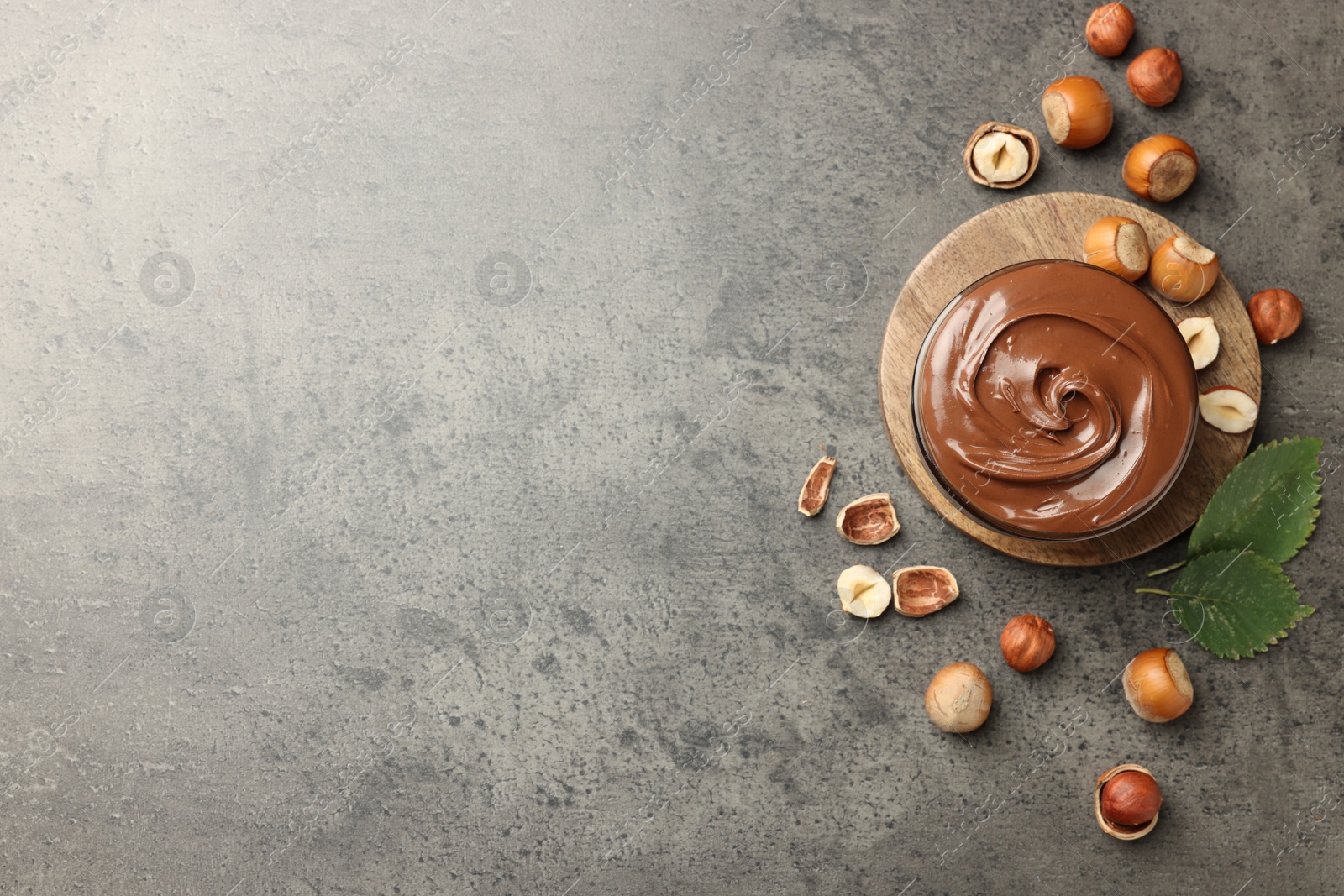 Photo of Tasty chocolate hazelnut spread and nuts on grey table, flat lay. Space for text