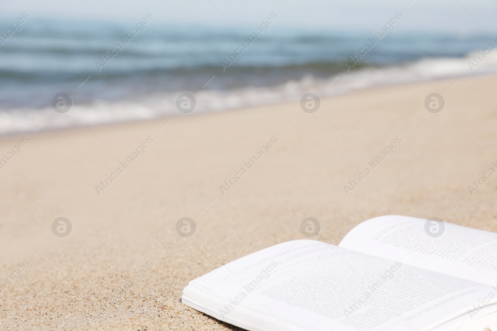 Photo of Open book on sandy beach near sea, closeup. Space for text