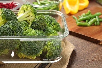 Photo of Container with broccoli on wooden table, closeup. Food storage
