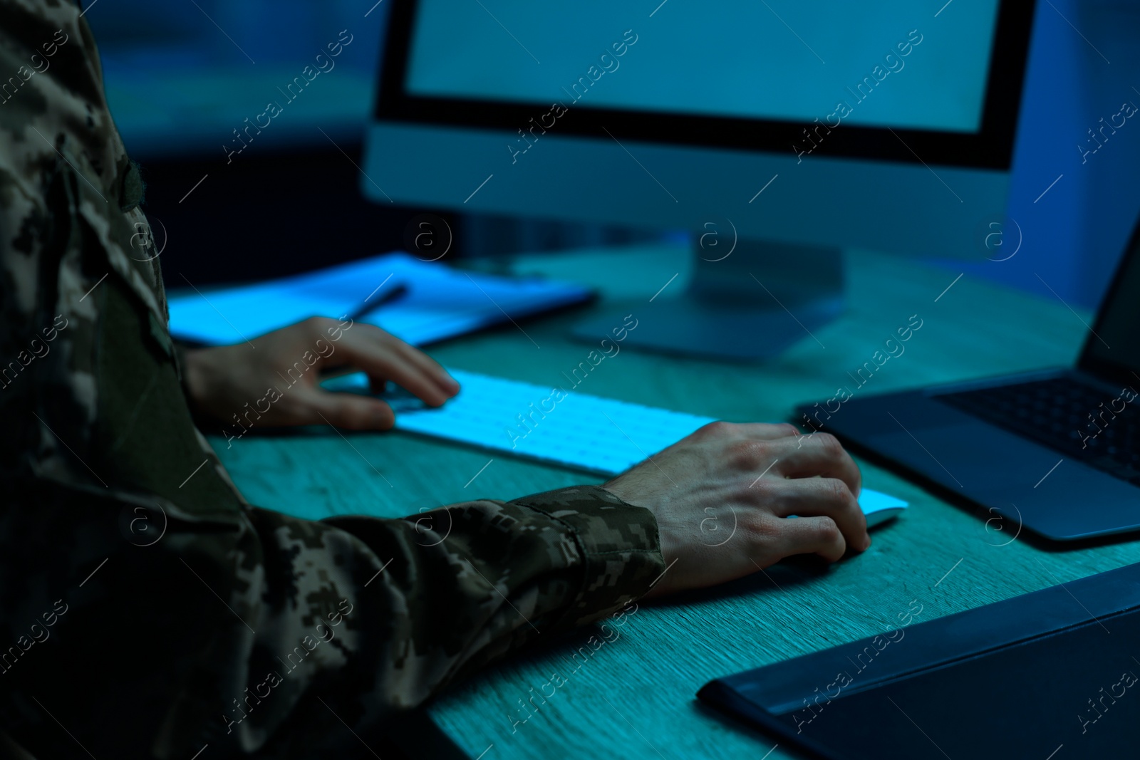 Image of Military service. Soldier working on computer at wooden table in office at night, closeup