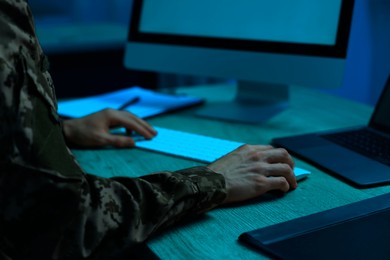 Image of Military service. Soldier working on computer at wooden table in office at night, closeup