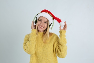 Happy woman with headphones on light grey background. Christmas music