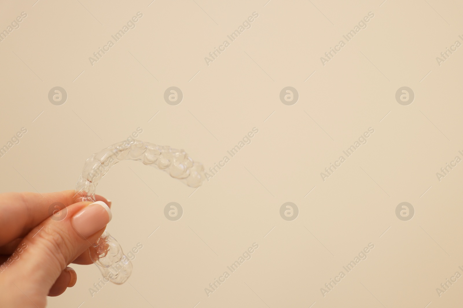 Photo of Woman with transparent dental aligner on beige background, closeup. Space for text