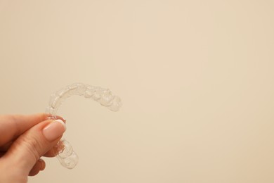 Photo of Woman with transparent dental aligner on beige background, closeup. Space for text