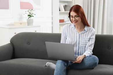 Happy woman using laptop on couch in room