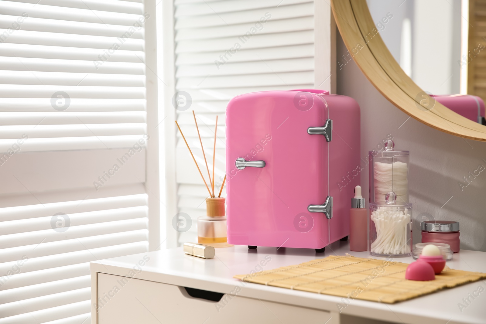 Photo of Cosmetics refrigerator and skin care products on white vanity table indoors