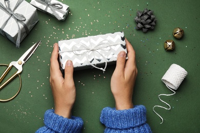 Photo of Young woman holding Christmas gift on green background, flat lay