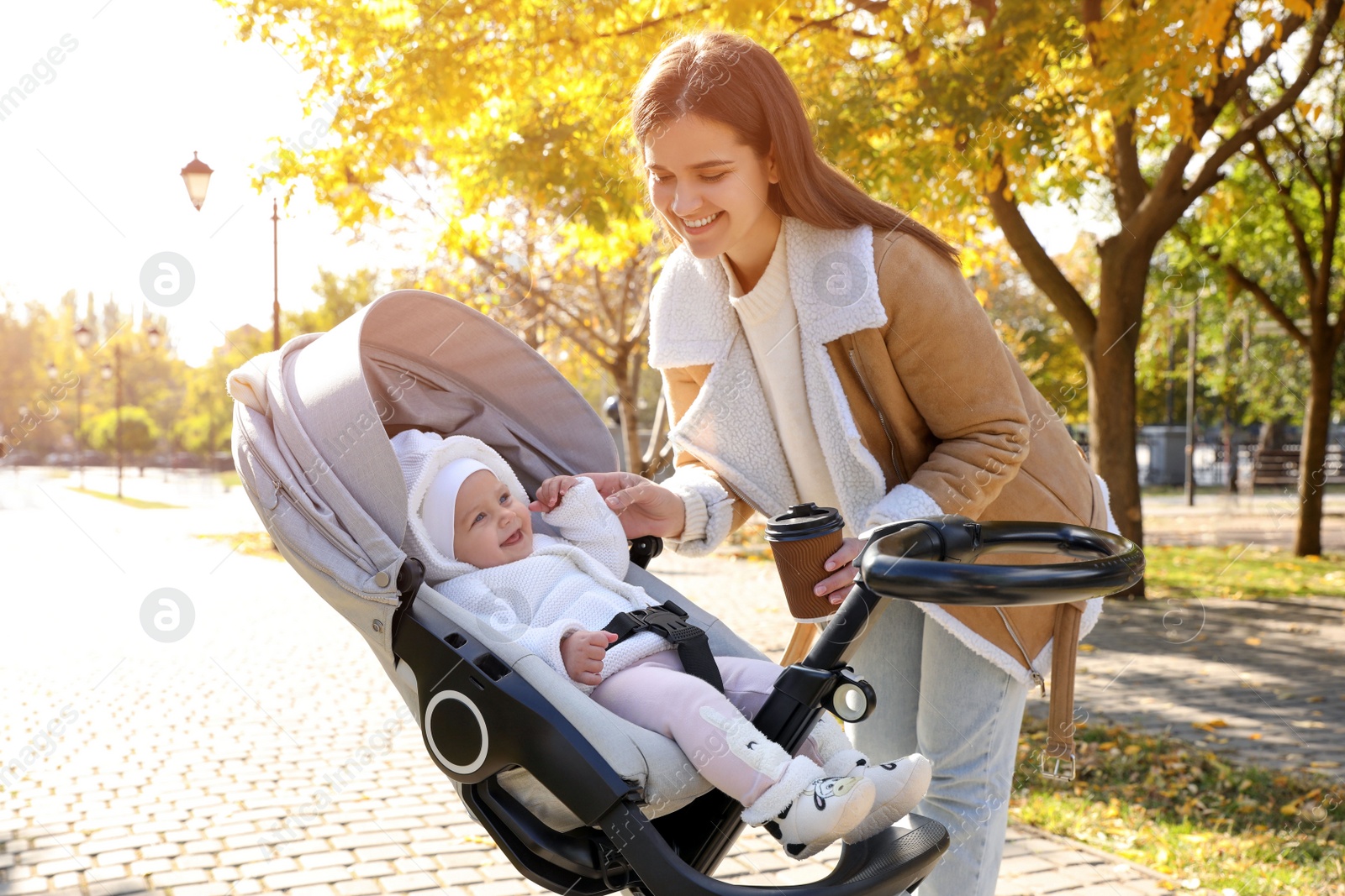 Photo of Happy mother with her baby daughter in stroller outdoors on autumn day