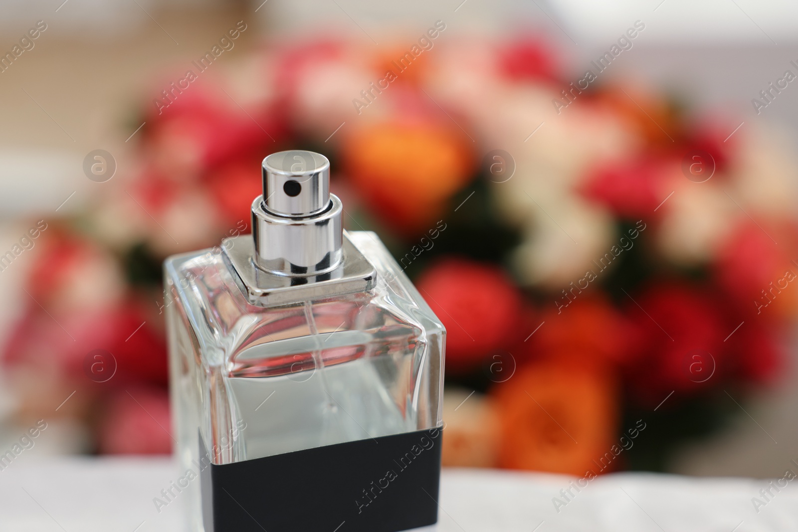 Photo of Bottle of perfume against beautiful roses, closeup. Space for text