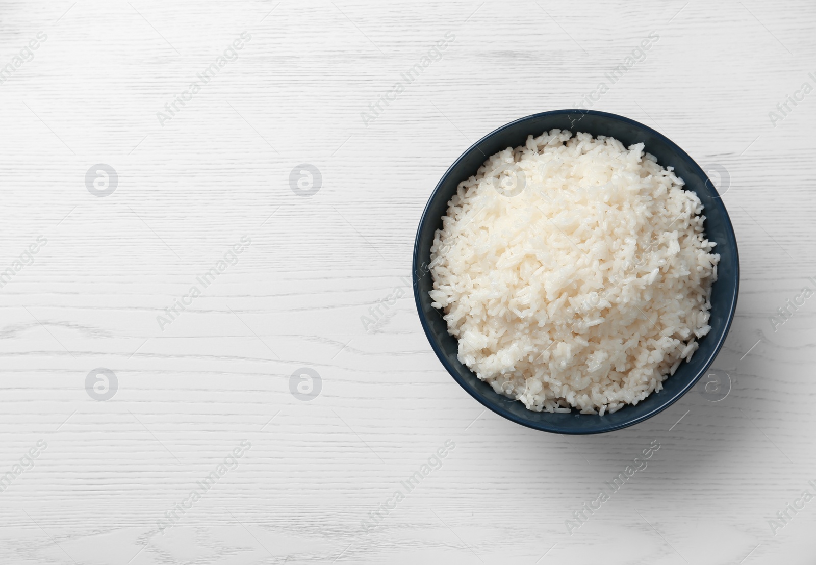 Photo of Bowl of boiled rice on wooden background, top view with space for text