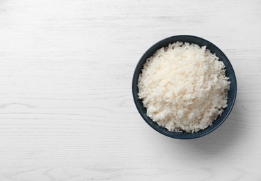 Photo of Bowl of boiled rice on wooden background, top view with space for text