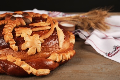 Photo of Fresh korovai on wooden table, closeup. Ukrainian bread and salt welcoming tradition