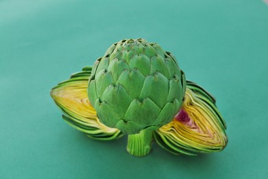 Photo of Cut and whole fresh raw artichokes on green background, closeup