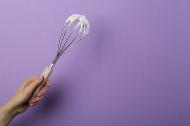 Photo of Woman holding whisk with whipped cream on violet background, closeup. Space for text