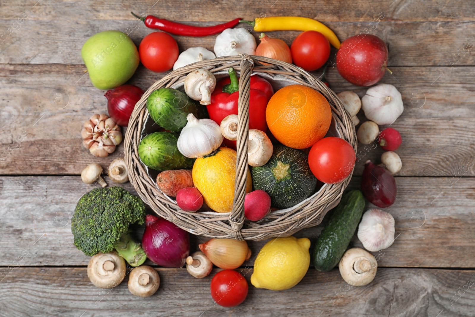 Photo of Basket with ripe fruits and vegetables on wooden table, top view